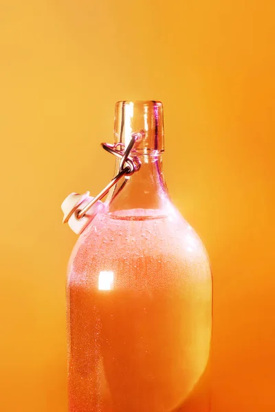 Skiner ljusa kylda glasflaska på en orange bakgrund. Sommarkoncept för rent sötvatten. — Stockfoto