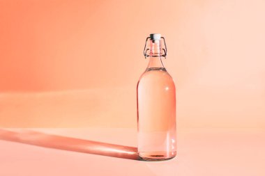 Güneş tarafından aydınlatılan temiz içme suyu dolu cam şişe. Metin için yeri olan pembe arkaplan.