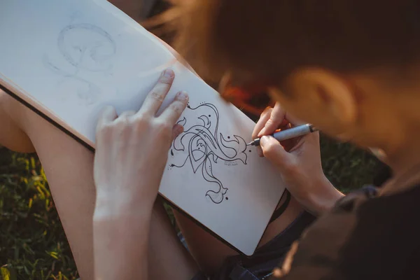 A mulher desenha cartas no parque. Delinear letras de mão em um caderno de esboços — Fotografia de Stock