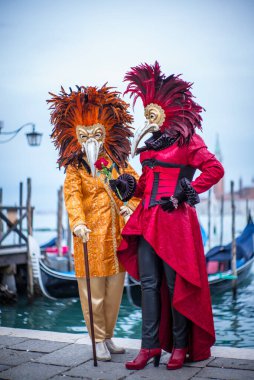 Venedik, İtalya - 7 Şubat 2018: Piazza San Marco 'da gondolların önünde renkli Venedik kostümlü ve maskeli kadınlar