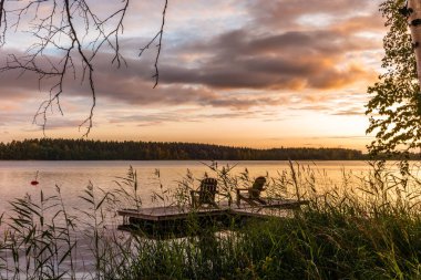 Finlandiya 'daki sakin Saimaa gölünün kıyısındaki iskelede, Sunset' te ahşap şezlonglar yanıyor. 