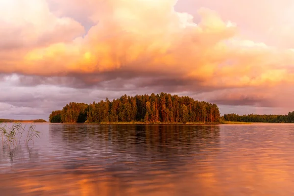 The shores of the calm Saimaa lake in Finland under a nordic sky on fire with a rainbow