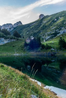Dağ kulübesi ve Alpstein dağ sırası güneş doğarken İsviçre kantonu Appenzell 'deki Faelensee Gölü' nü yansıtıyor.