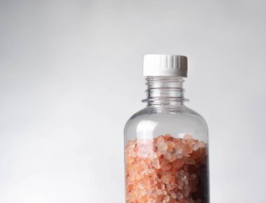 Siyah bir masada, berrak bir şişedeki pembe tuz kristalleri. Spa konsepti.