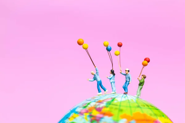 迷你的人 快乐的家庭手持气球在全球与粉红色背景和复制空间文本 — 图库照片