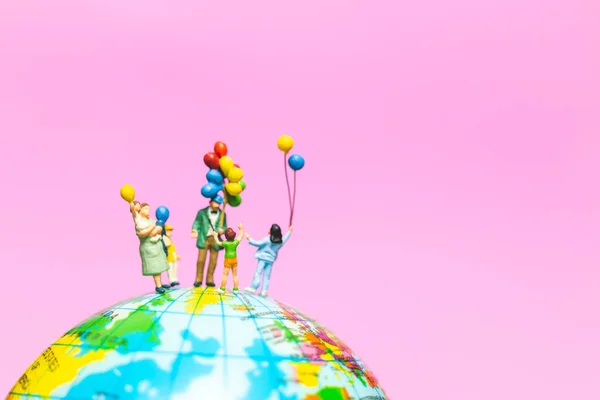 迷你的人 快乐的家庭手持气球在全球与粉红色背景和复制空间文本 — 图库照片