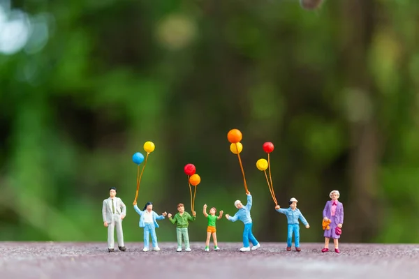 Pessoas em miniatura: família feliz segurando balões coloridos — Fotografia de Stock