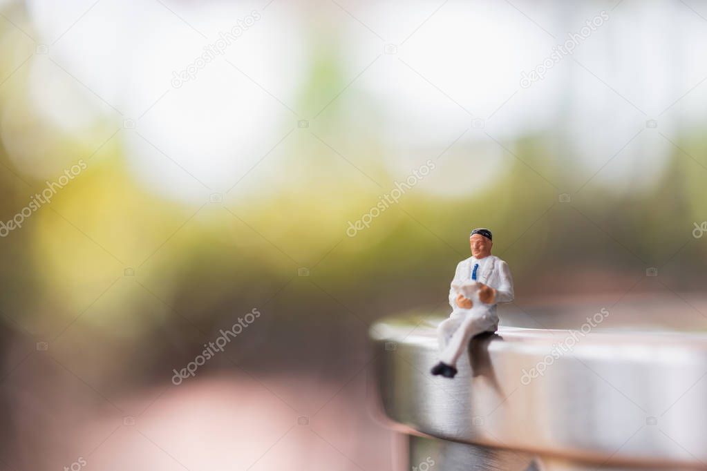 Miniature people: Businessman sitting  reading book outdoor