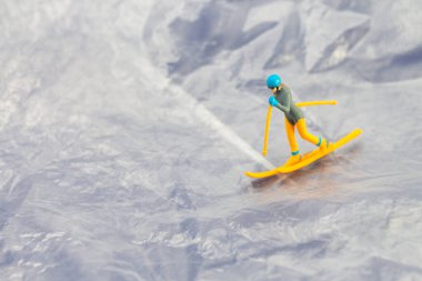 Karlı bir dağ manzarasında kayak yapan küçük bir heykelciğin yaratıcı konsept görüntüsü macera ve kış sporlarını sembolize ediyor..
