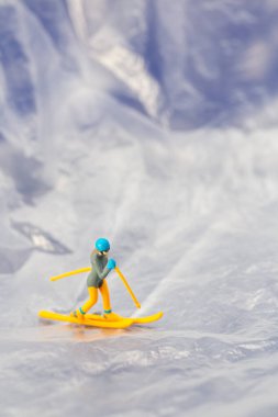 Karlı bir dağ manzarasında kayak yapan küçük bir heykelciğin yaratıcı konsept görüntüsü macera ve kış sporlarını sembolize ediyor..