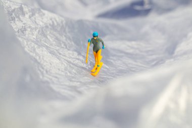 Karlı bir dağ manzarasında kayak yapan küçük bir heykelciğin yaratıcı konsept görüntüsü macera ve kış sporlarını sembolize ediyor..