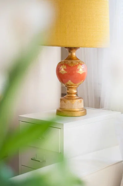 A yellow golden decorative lamp behind a blurry peace lily plant
