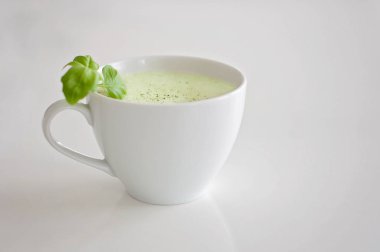 Sağlıklı yeşil çay matcha latte fesleğen ve köpük üst - beyin fonksiyonları artırmak için sıcak bir içecek ve kanserden korunma olarak süslenmiş beyaz çay bardağı soya ve yulaf sütlü!