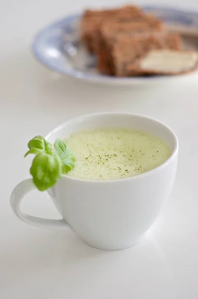 Gezonde groene thee matcha latte met soja en haver melk in een kopje witte thee versierd met basilicum en schuim bovenop - een warme drank te stimuleren van hersenfunctie en als een kankerpreventie! Knäckebröd en boter op achtergrond wazig — Stockfoto