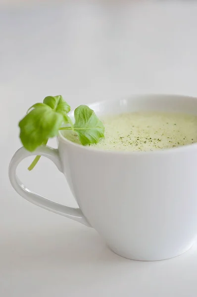 Υγιή πράσινο τσάι latte matcha με σόγια και βρώμη γάλα σε ένα φλιτζάνι λευκό τσάι διακοσμημένα με βασιλικό και αφρό στην κορυφή - ένα ζεστό ρόφημα να ενισχύσει τη λειτουργία του εγκεφάλου και ως πρόληψη του καρκίνου! — Φωτογραφία Αρχείου