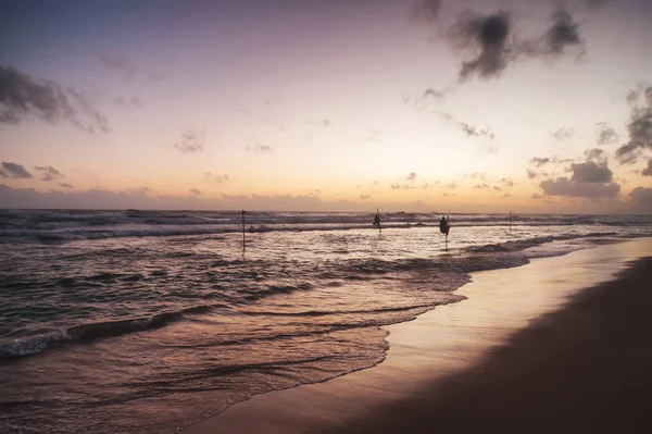 Океанський пляж на заході сонця з тристоронніми рибалками на горизонті — стокове фото