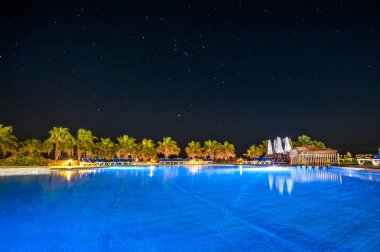 Egzotik okyanusun kıyılarında açık havuz ve suda palmiye ağaçlarının yansıması. Yaz manzarası. Gece manzarası.