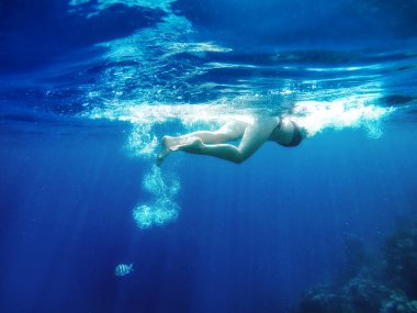 Mavi okyanusta şnorkelle dalış yapan bir adamın manzaralı sualtı görüntüsü.