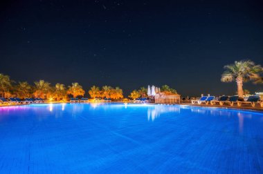Egzotik okyanusun kıyılarında açık havuz ve suda palmiye ağaçlarının yansıması. Yaz manzarası. Gece manzarası.