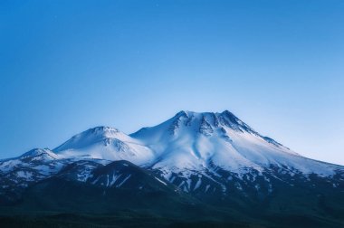 Karla kaplı yanardağı ve bir dağ gölünde yansıması olan doğal bir arka plan.