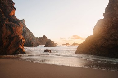 Portekiz, Sintra 'daki Praia da Ursa' nın görkemli kayalıkları ve altın kumları sakin bir günbatımı sırasında çarpıcı kaya oluşumlarına çarpar.