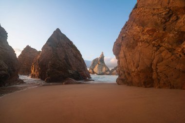 Portekiz, Sintra 'daki Praia da Ursa' nın görkemli kayalıkları ve altın kumları sakin bir günbatımı sırasında çarpıcı kaya oluşumlarına çarpar.