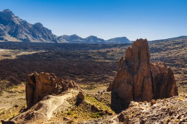 Tenerife 'deki Teide Ulusal Parkı' nın dramatik manzaralarını keşfedin, berrak mavi gökyüzü altında engebeli volkanik oluşumlar ve canlı bitkiler gösterin. Kanarya Adaları, İspanya.