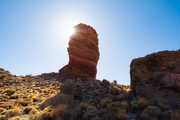Потрясающий вид на Roque Cinchado, возвышающийся над пересеченной местностью, а гора Тейде величественно возвышается на заднем плане в ясный день Национальный парк Тейде, Тенерифе, Канарские острова, Испания.