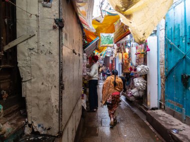 Varanasi, Uttar Pradesh, Hindistan - Şubat 2015: Eski şehirde dükkanlarla dolu dar bir sokakta yürüyen bir kadın.