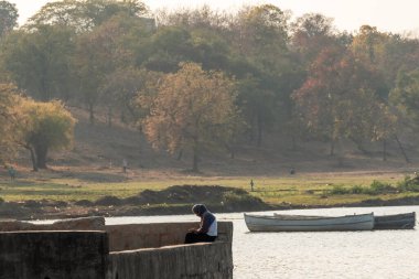 Nagpur, Maharahstra, Hindistan - Mart 2019: Peçe takmış genç bir Hintli kız şehirde Futala gölünün güzel manzarasında tek başına oturuyor.