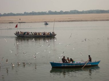 Varanasi, Uttar Pradesh, Hindistan - Şubat 2015: Seyyahlar Ganga nehrinde ahşap botlara binip etrafta kuşlar uçuşuyor.