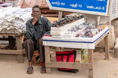 Chennai, Tamil Nadu, Hindistan - Ağustos 2018: Yüzünde tuhaf bir ifadeyle asfalt dükkanının yanında oturan Hintli bir sokak satıcısı.