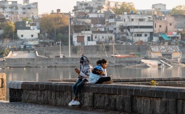 Nagpur, Maharahstra, Hindistan - Mart 2019: Göl kenarındaki akıllı telefonlarına bakan iki genç Hintli kadın.