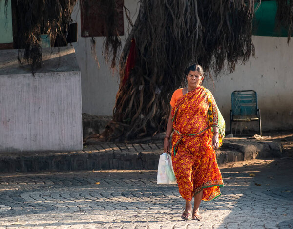 Nagpur, Maharashtra, India - March 2019: An Indian woman wearing a bright red sari walking on the street.