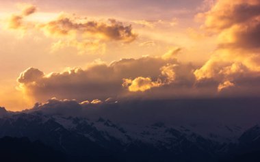 Güneş ışınları Hindistan 'ın HImachal Pradesh kentindeki Sarahan köyündeki Himalaya Dağları' nın karla kaplı bir sıradağından bulutların arasından akar..