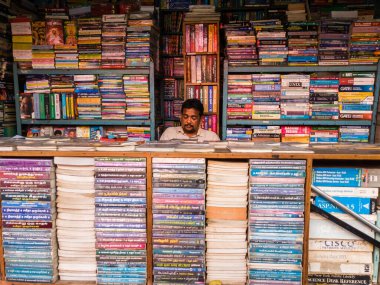 Trichy, Tamil Nadu, Hindistan - Şubat 2020: Akademik kitap yığınlarıyla dolu bir dükkanda oturan bir kitap satıcısı.