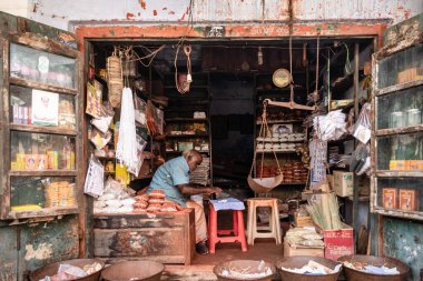 Trichy, Tamil Nadu, Hindistan - Şubat 2020: Eski, pis bir dükkanda oturan Hintli bir esnaf yiyecek ve çeşitli bakkaliye ürünleri satıyor.