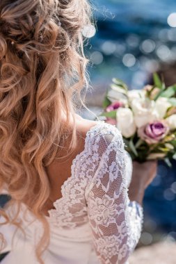 Deniz kenarında buketi olan lüks gelinlik içinde güzel bir gelin. Deniz kenarında düğün..