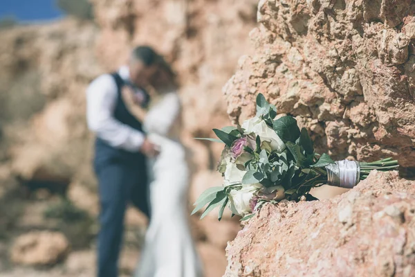 Taşın üzerinde yeşil ve beyaz çiçeklerden bir buket gelin ve damat arka planda. — Stok fotoğraf