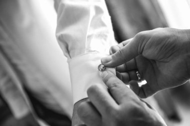 Damadın kol düğmelerini takmasına yardımcı olur. Yakın çekim, düğün günü.