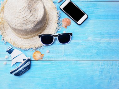 Tatil tatil arka plan. Kopya alanı ile mavi ahşap üzerine hasır şapka, güneş gözlüğü, kabukları ve smartphone üstten görünüm. 