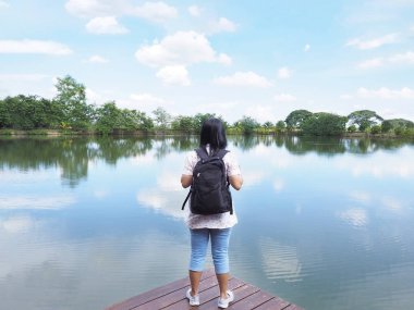 Arkadan görünüşü Asyalı kadın backpacker turist ahşap iskelede nehir ve mavi gökyüzü arka plan önünde tutuyoruz. Tatil kavramı kopya alanı ile beraber seyahat.