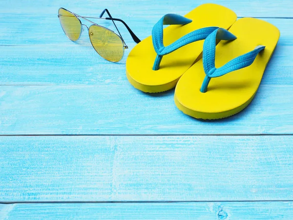 Üstten Görünüm sarı kauçuk flip flop Ayakkabı ve güneş gözlüğü kopya alanı ile mavi ahşap arka plan üzerinde. Yaz tatil tatil kavramı.