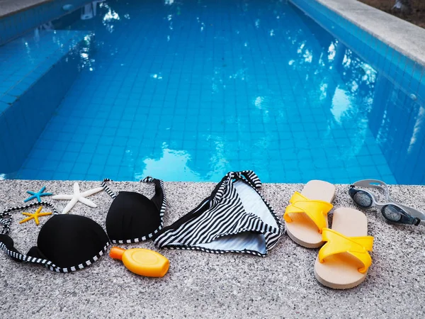 Woman swimming suit and accessories on edge of swimming pool.