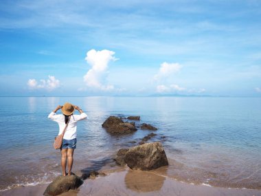 Kayanın üzerinde duran ve bakan mutlu genç kadının geri görünümü 
