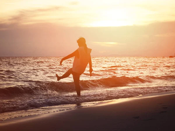 Silueta sonriente mujer pateando ola de agua en la playa . — Foto de Stock