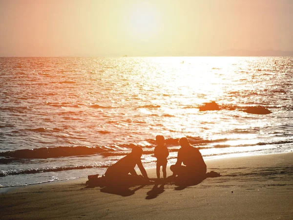 Silhouette happy family playing with sand on summer sunset beach — Stock Photo, Image