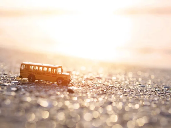 Close up yellow school bus toy on sand at sunset beach. — Stock Photo, Image