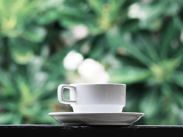 Vit kopp kaffe över grön blommig abstrakt oskärpa bakgrund. — Stockfoto