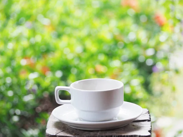 Vit kopp kaffe över grön blommig abstrakt oskärpa bakgrund. — Stockfoto